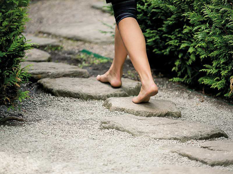 Nackte Füße laufen über einen Naturstein-Gartenweg.