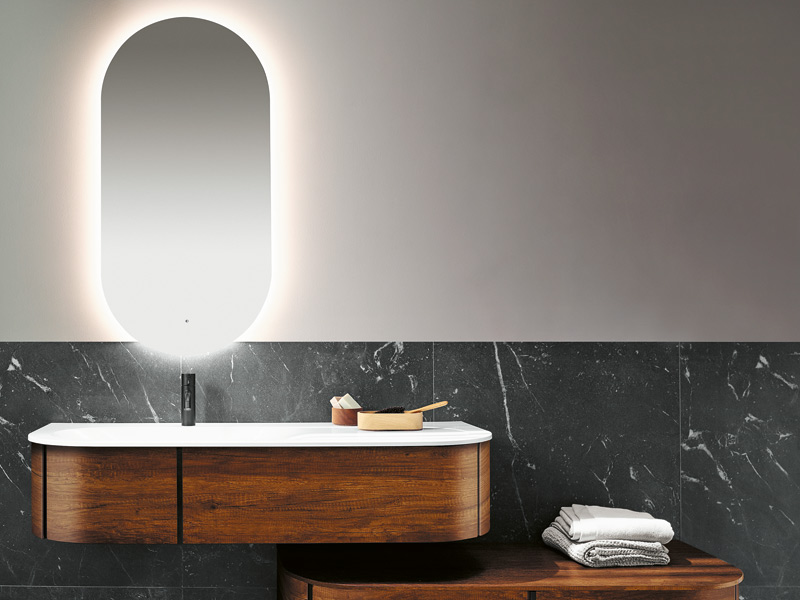 Ovaler beleuchteter Badspiegel über einem Waschtisch in Holzdekor von burgbad
