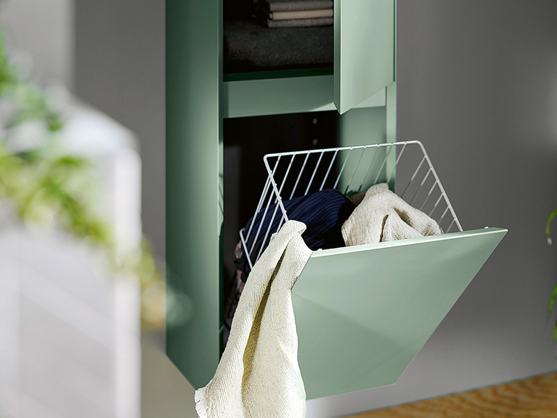 grüner Badhochschrank mit integriertem Wäschekorb aus Metall und darin befindlicher Wäsche