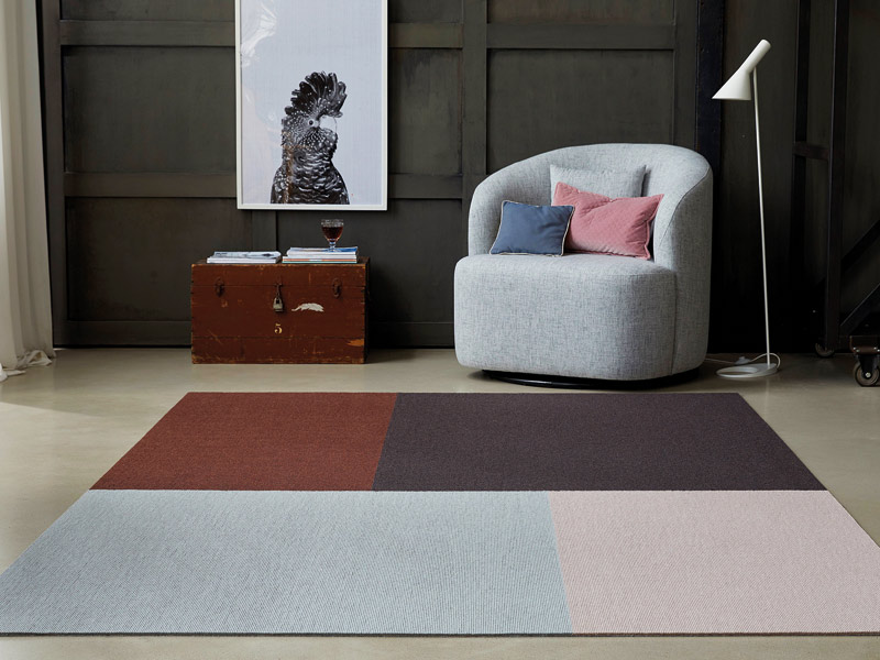 Bodenbelag Teppich in ier Farben auf Fliesenboden mit Sessel im Hintergrund
