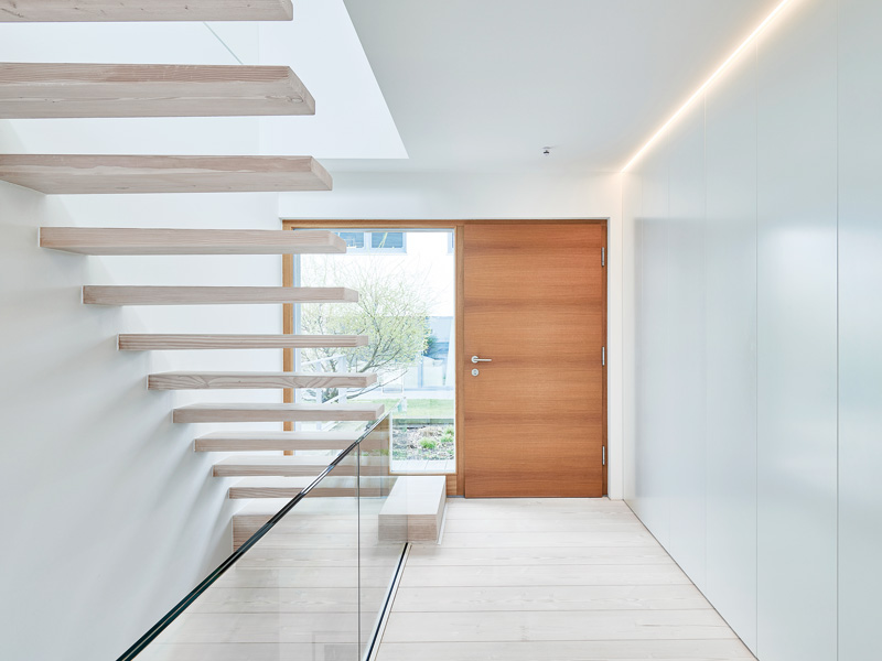 Entwurf Wittlinger von Baufritz - schwebende Treppe im hellen Flur und Blick auf die Eingangstür