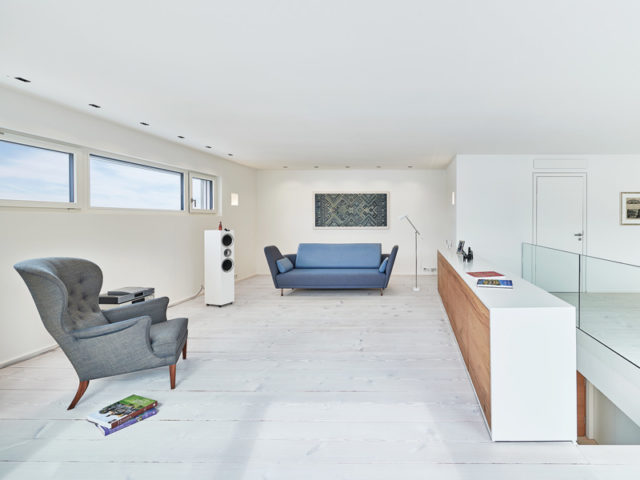 Entwurf Wittlinger von Baufritz - Wohnbereich mit weißem Fußboden, blauer Couch und grauem Sessel
