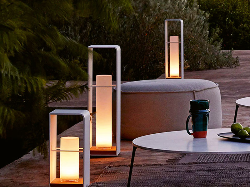 Gartenbeleuchtung Ideen mit Solarleuchten von Lightzey. Drei Stück stehen leuchtend auf einer Terrasse neben Sitzhocker und Tischen.