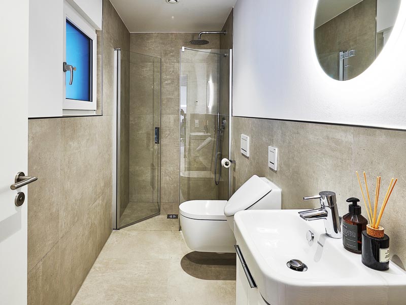 Gästebad lang mit Dusche, WC, Urinal und Waschtisch und edlen großen Fliesen im Musterhaus Balance