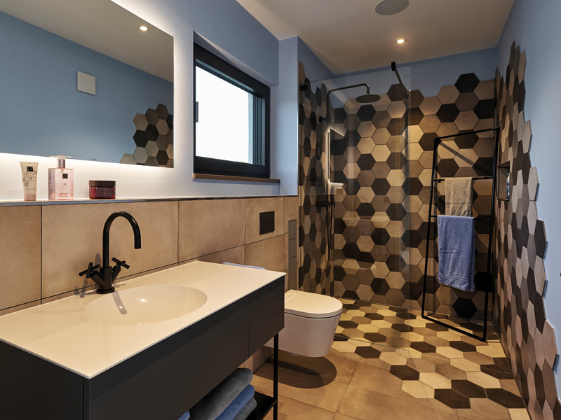 Gästebad mit Dusche, Waschtisch und WC und ausgefallenen Fliesen im Duschbereich im Musterhaus Core