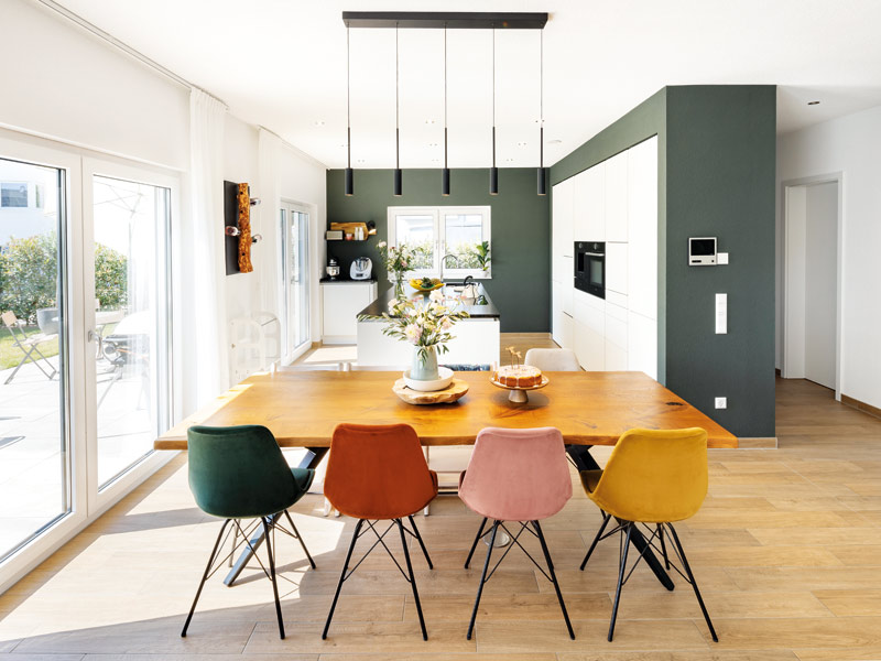Stadtvilla Medley 3.0 300 B von Fingerhaus - Essbereich mit großem Holztisch und farbigen Stühlen und Blick in die offene Küche