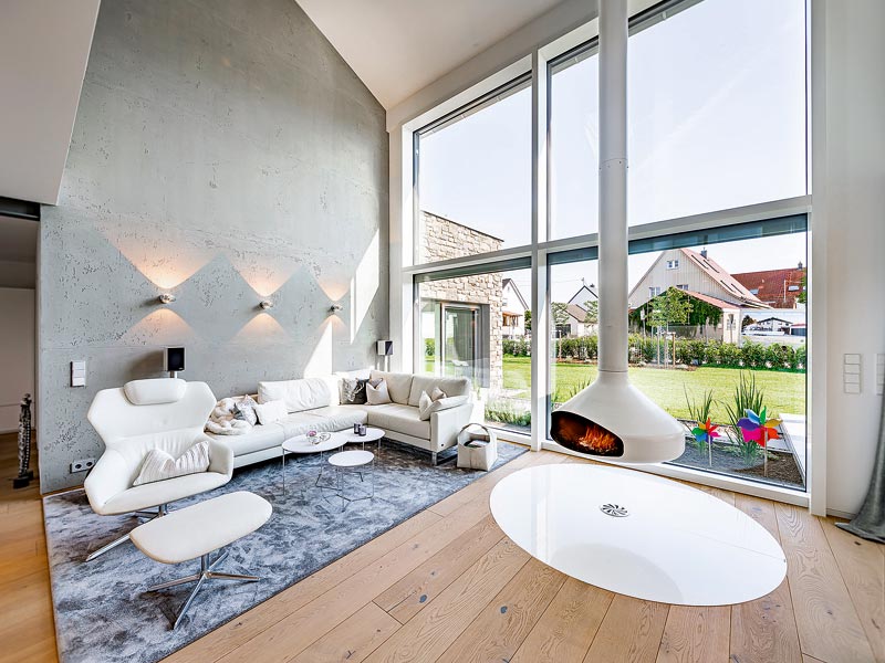 modernes Wohnzimmer mit weißer Couchlandschaft und hängendem Kamin vor großen Panoramafenstern