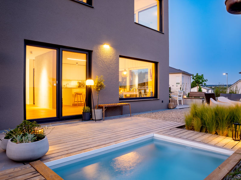 Luxhaus Satteldach Landhaus 138 Aussenansicht der Terrasse mit Pool bei Abendbeleuchtung