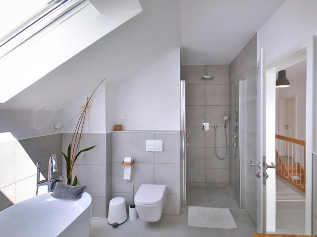 helles Badezimmermit freistehender Wanne unter einem Dachflächenfenster und WC und Dusche dahinter