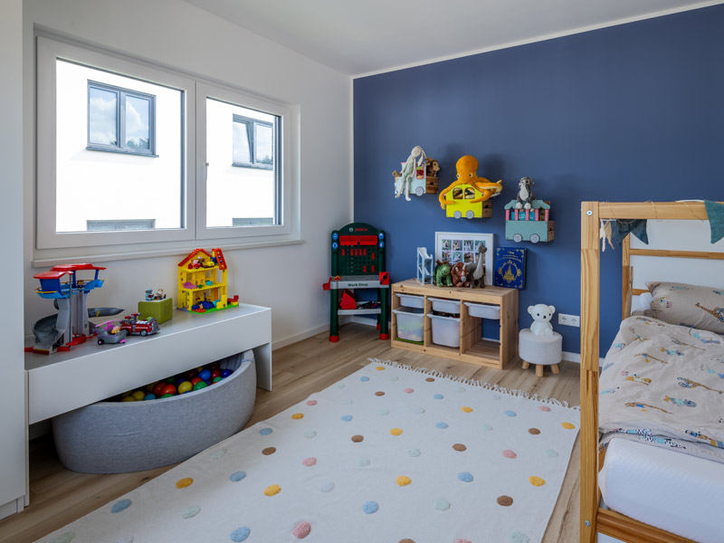 LUXHAUS Walmdach 169 Kinderzimmer mit einer blauen Wand und Teppich mit bunten Punkten auf dem Boden