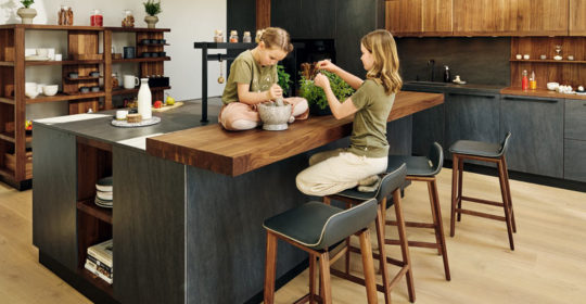 2 Mädchen sitzen auf der Arbeitsplatte und einem Stuhl in einer schicken Küche und mörsern Kräuter