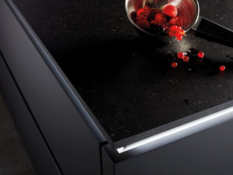 Ein Metallsieb mit roten Früchten fällt auf eine schwarze Arbeitsplatte, mit der fällt es leicht eine Küche nachhaltig einzurichten, da aus recyceltem Material.
