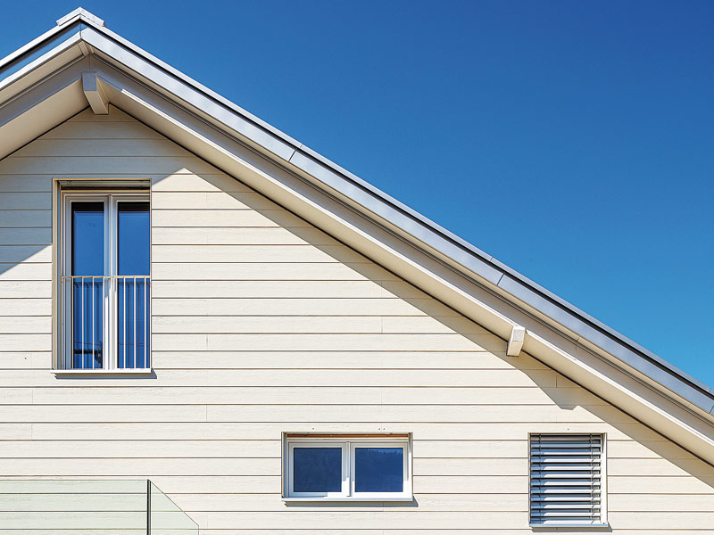 Ausschnitt eines Satteldachhauses mit cremefarbenen Faserzementplatten an der Fassade.