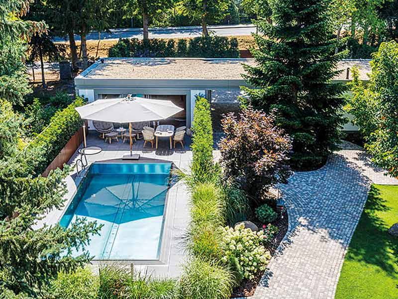 Gartenbereich mit Pool und Poolhaus bei strahlendem Sonnenschein