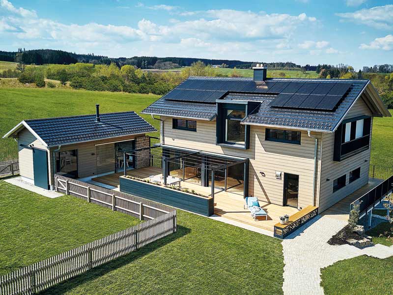 Musterhaus Heimat 4.0 von Baufritz Aussenansicht mit Haupthaus und Terrasse und Backhaus mit Hühnerstall daneben.