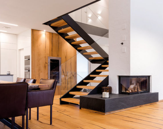 Koch- und Wohnbereich mit Treppe aus Holz, Stahl und Glas neben einem Kamin in der teilenden Wand