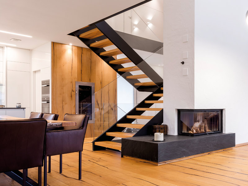 Koch- und Wohnbereich mit Treppe aus Holz, Stahl und Glas neben einem Kamin in der teilenden Wand