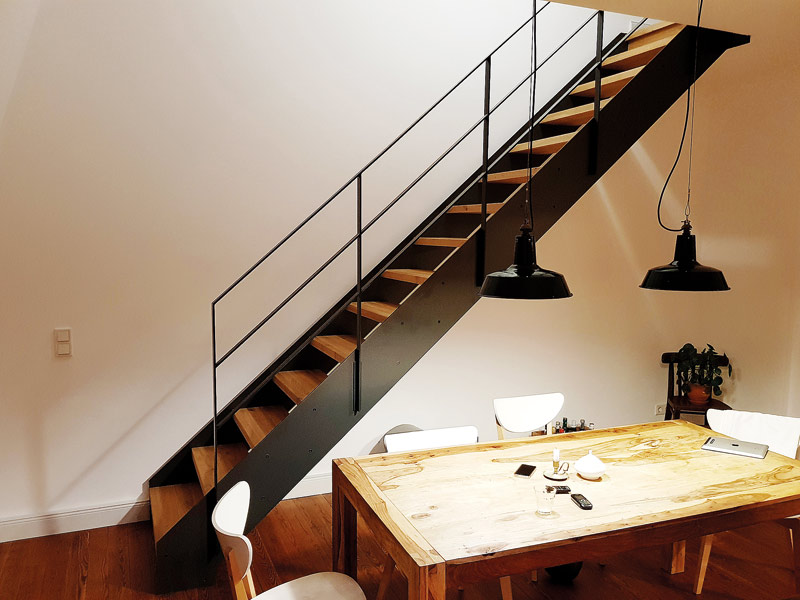 Steile Treppe hinter einem Esstisch aus Stahl und Holz im Industrial Style