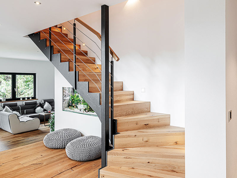 Treppe aus Holz und Stahl ins Obergeschoss führend mit einem in die Wand darunter eingebauten Aquarium