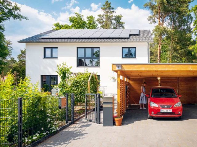 WeberHaus generation 5.5 Aussenansicht zur Straße mit Holzcarport davor und gut erkennbarer Photovoltaikanlage auf dem Satteldach des Hauses