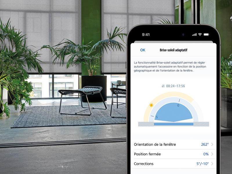 Innenrollos in einem loftartigen Raum, die per Handy-App gesteuert werden können. App auf französisch.