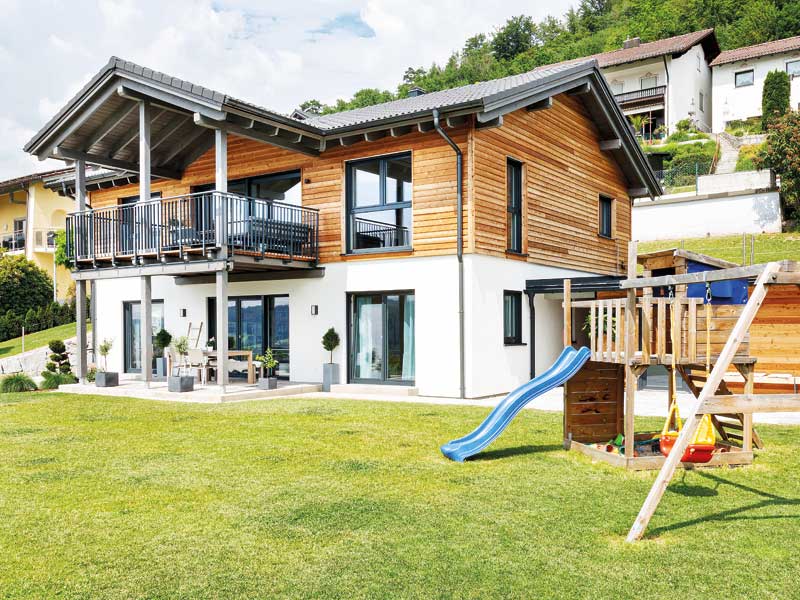 Hanghaus in Niederbayern von Wolf System oben mit Holz und unten mit Putz verkleidet mit großem Balkon über der Terrasse