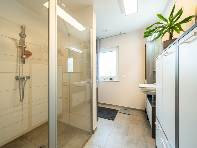 Bungalow mit Doppelgarage von Streif Haus, Badezimmer, linker Hand große Walk-In-Dusche, gegenüber Badschränke mit viel Stauraum, dahinter Waschbecken mit Waschtisch