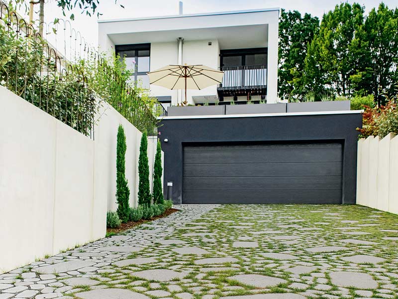 Zufahrten und Wege: Zufahrt zu einer Doppelgarage mit begrünten Fugen, und Einfamilienhaus mit Terrasse im Hintergrund.