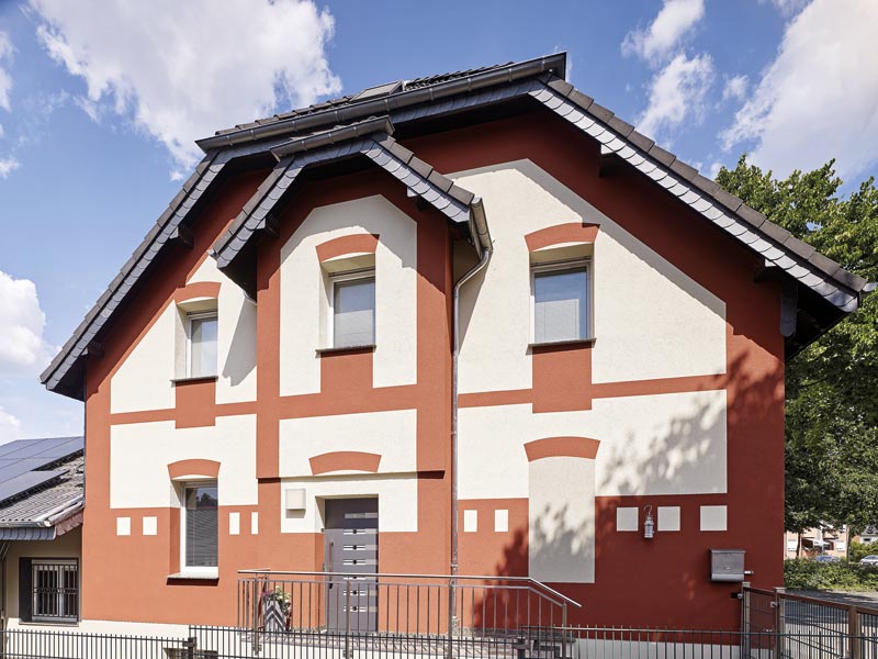 Saniertes Einfamilienhaus mit neuer zweifarbiger Fassade in rot-weiß und einem Briefkasten außen dran.