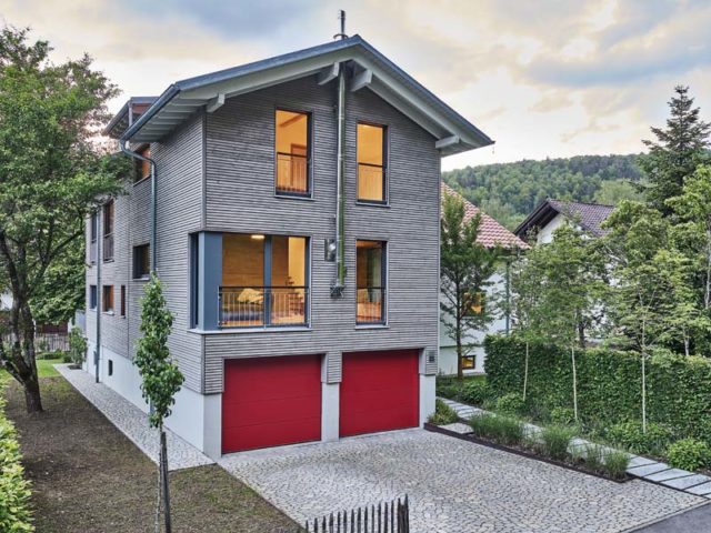 Schicker Neubau mit grauem Holz verkleidet und roten Garagentoren. Haus Bienert von Baufritz.