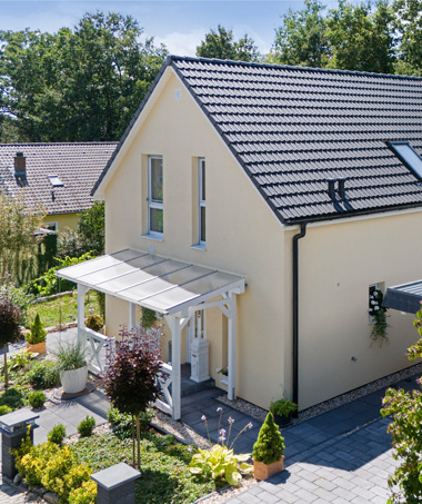 Zweistöckiges Einfamilienhaus mit gelber Fassade, Satteldach und einem überdachten Eingangsbereich, umgeben von gepflegtem Garten und gepflastertem Weg.