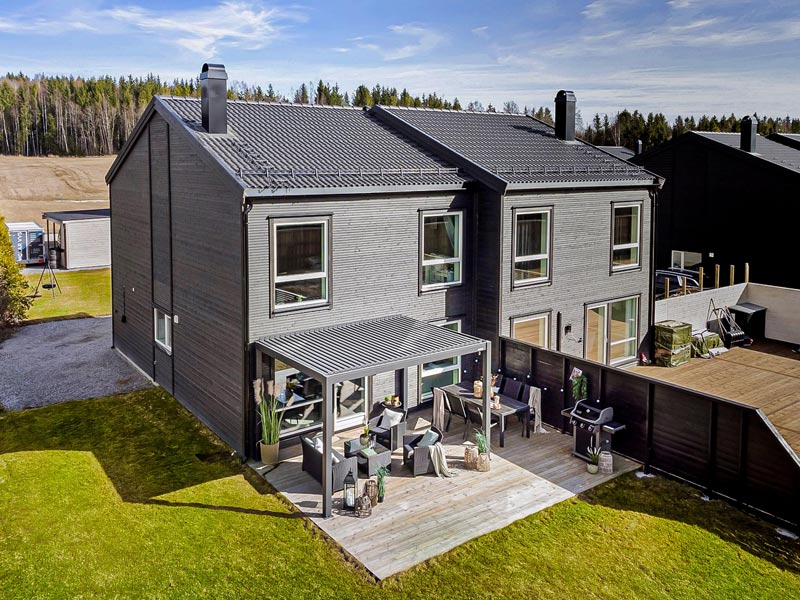 Holzdoppelhaus dunkel verkleidet mit einer Pergolux Pergola S2 auf einer Seite über der Terrasse